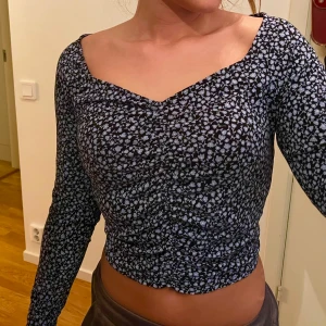 Blommig långärmad topp från Monki - Säljer en söt blommig topp från Monki med långa ärmar och v-ringad hals. Toppen har en svart bas med vita blommor och rynkade detaljer för en fin passform🌸
