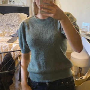 Söt stickad tröja - Säljer en mysig grön stickad tröja med korta ärmar. Perfekt för en avslappnad stil och passar bra till jeans. Tröjan har en rund halsringning och ribbade kanter.