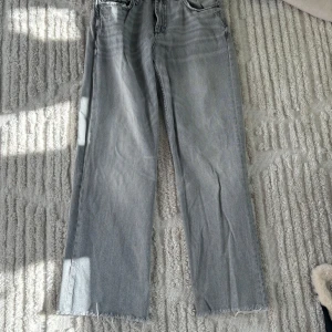 Grå jeansbyxor från Zara - Snygga grå jeansbyxor från Zara i storlek L. Byxorna har en rak passform och är medel höga med fransade kanter vid bensluten. Perfekt för dig som vill gå upp en storlek till dom perfekta baggy jeansen 