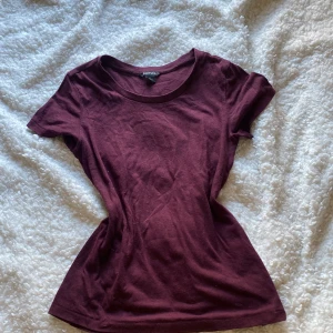 Vinröd t-shirt från Monki - Säljer en stilren vinröd t-shirt från Monki i storlek XS. Den har en klassisk rund hals och korta ärmar, perfekt för en avslappnad look. Materialet känns mjukt och bekvämt mot huden. Passar perfekt till jeans eller kjol för en enkel och snygg outfit.