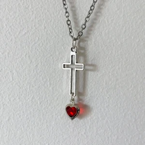 Silverhalsband med kors och rött hjärta - Elegant silverhalsband med ett korshänge och ett rött hjärta. Perfekt för att ge en stilren touch till din outfit. Kedjan är tunn och smidig, vilket gör den bekväm att bära hela dagen.
