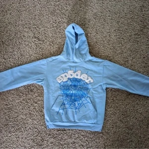 Sp5der hoodie baby blue - Säljer en cool ljusblå hoodie med en unik spindelnätsdesign och texten 'sp5der' på framsidan. Perfekt för en avslappnad stil. Tillverkad i mjuk bomull för extra komfort. Passar perfekt för höst och vår.