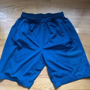 Blå shorts från Adidas - Snygga blå shorts från Adidas med elastisk midja och sidofickor. Perfekta för träning eller en avslappnad dag. Adidas-loggan syns diskret på benet. 