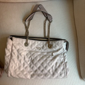 Vit quiltad axelväska - Vit quiltad axelväska från Guess med kedjehandtag och dragkedja. Väskan kommer med en tillhörande liten plånbok.