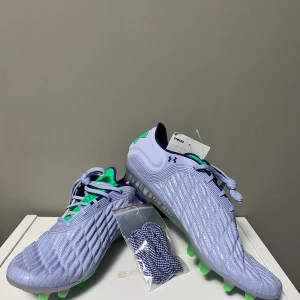 Under armor magnetic clone elit 3.0 - Snygga ljuslila fotbollsskor från Under Armour med grön och mörkblå detaljering. Skorna har en strukturerad yta och snörning för optimal passform. Perfekta för fotbollsplanen med sina gröna dobbar för bra grepp. (Skick: Helt nya med prislapp!) (priset kan diskuteras!)