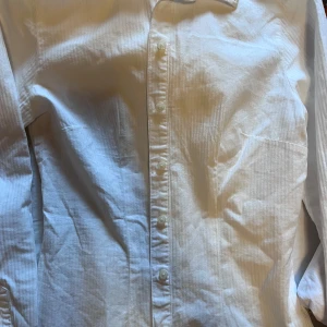 Vit randig skjorta från Brandy Melville - Säljer en stilren vit skjorta från Brandy Melville med diskreta ränder. Skjortan har en klassisk krage och knappar framtill. Perfekt för en chic och avslappnad look.