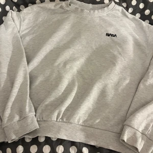 Grå sweatshirt med NASA-logga - Säljer en grå sweatshirt med en liten NASA-logga på bröstet. Tröjan har långa ärmar och ribbade muddar vid ärmslut och nederkant. Perfekt för en avslappnad stil! 🚀