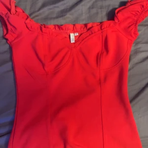 Röd topp med volangdetaljer - Snygg röd klänning med volangdetaljer vid axlarna. Den har en smickrande passform och korta ärmar. Perfekt för en kväll ute eller en speciell tillställning. 💃