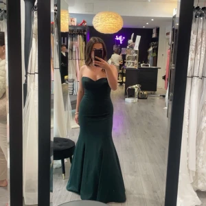 Mörkgrön axelbandslös långklänning - Säljer en elegant mörkgrön axelbandslös långklänning med en figurnära passform. Perfekt för en speciell kväll eller fest. Använd en gång på min bal, och har ingen defekt. Jag är 160 mc lång och klänningen är några cm längre än det. Nypris: 3700kr. Pris kan förhandlas!!