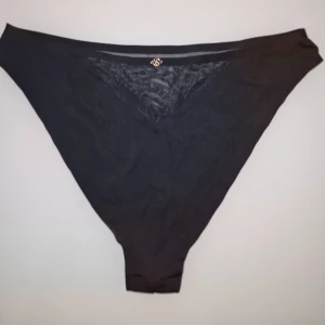 Svart spetstrosa från Victoria's Secret  - Elegant svart trosa med spetsdetaljer. Den har en diskret logga i guld och är tillverkad i ett mjukt och bekvämt material.