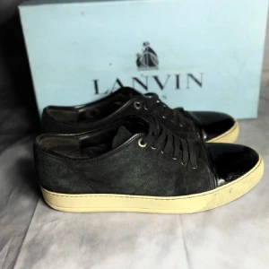 Svarta sneakers från Lanvin - Snygga svarta sneakers från Lanvin med en stilren design. Riktigt sköna skor som är i ett bra skick men tyvärr lite sönder på vänster sko. extra snören och box ingår. Priset är diskuterbart!!!