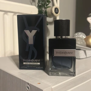 Yves Saint Laurent Eau de Parfum - Säljer en elegant Yves Saint Laurent Eau de Parfum i en stilren svart flaska med silverdetaljer. Flaskan rymmer 60 ml och har en lyxig känsla med märkets logotyp på locket. Perfekt för den som vill ha en sofistikerad doft. Helt ny, sprayad 3 gånger. Pris kan ändras 