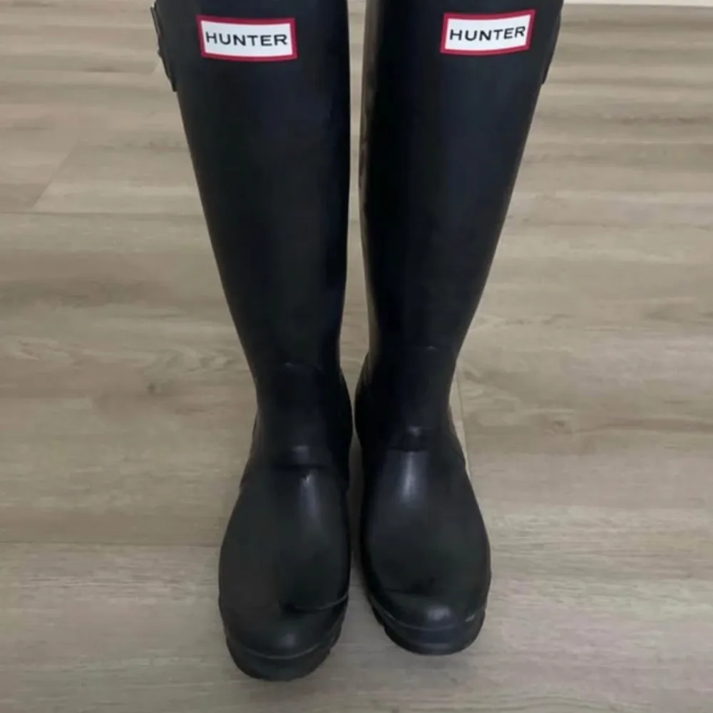 Snygga svarta stövlar från Hunter, perfekta för regniga dagar. De har en klassisk design med justerbart spänne på sidan och Hunter-loggan framtill. Insidan har ett mönstrat foder för extra komfort.. Kengät.
