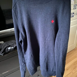 Mörkblå tröja från Morris - Säljer en stilren mörkblå tröja från Morris i 100% merinoull. Tröjan har en liten röd broderad detalj på bröstet och långa ärmar. Använd fåtal gånger.