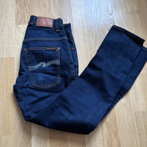 Mörkblå jeans från Nudie Jeans - Snygga mörkblå jeans från Nudie Jeans med klassisk femficksdesign och orange sömmar. Jeansen har en normal passform och är tillverkade i högkvalitativt denim. Perfekta för en stilren look. Storleken är 32 32 och är i modellen Thin Finn och sitter lite tajtare och passar någon som är runt 170 cm. Skick 9/10 💯och använd ett fåtal gånger bara någon tråd sticker ut. Hör av vid frågor och funderingar 🙏