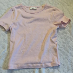 Ljusrosa topp  - Säljer en ljusrosa topp från Gina Tricot, basically basics-kollektionen. Den är kortärmad och gjord i mjuk bomull, perfekt för en avslappnad stil. Enkel och stilren design som funkar till det mesta. 