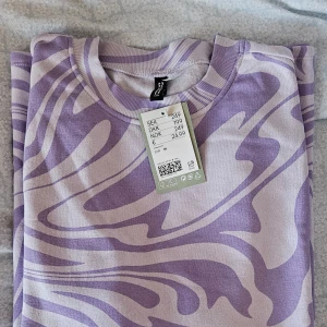 Lila mönstrad tröja från Divided - Säljer en cool lila långtröja från Divided med ett unikt mönster. Tröjan är tillverkad av 34% återvunnen bomull och 40% återvunnen polyester. Perfekt för dig som vill ha en stilren look med en twist. 🌟 