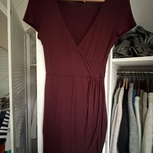 Vinröd klänning från NLY One - Snygg vinröd klänning från NLY One med v-ringad design och korta ärmar. Perfekt för en stilren look. Klänningen har en omlottstil som ger en elegant touch.