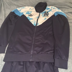 Blå tracksuit från Puma och Marseille - Säljer en snygg tracksuit från Puma och Marseille. Inte kommit till användning. Helt oanvänd i storlek L. Hör av vid frågor!
