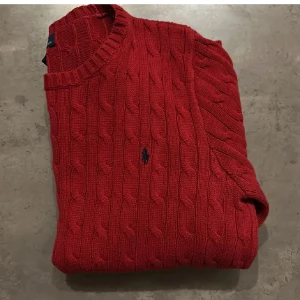 Röd kabelstickad tröja från Polo Ralph Lauren - Säljer en fett snygg röd kabelstickad tröja från Polo Ralph Lauren. Tröjan har långa ärmar och en rund halsringning. Storleken är M men passar även på S. Tvär fet och inga tecken på användning.