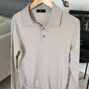 Beige långärmad pikétröja från Mango - Snygg beige långärmad pikétröja från Mango med klassisk krage och knappar framtill. Perfekt för en stilren och avslappnad look. Passar bra till både jeans och chinos. Är storlek M men sitter som S