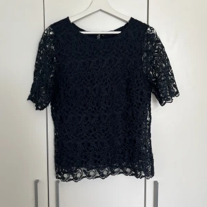 Marinblå spetsblus från Signature - Säljer en elegant marinblå spetsblus från Signature. Blusen har korta ärmar och ett vackert spetsmönster som ger en stilren look. Perfekt för att lyfta vilken outfit som helst. 💙Storlek M men passar även mig S