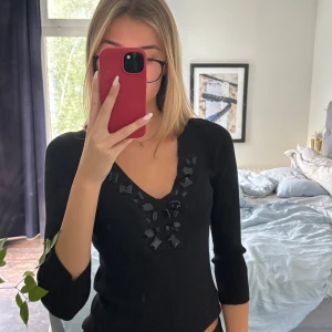 Svart topp med pärldetaljer - Svart topp med v-ringning och coola svarta pärldetaljer runt halsen. Modellen är croppad och har trekvartsärm, vilket ger en trendig och stilren look. Skirv vid funderingar!💞💞