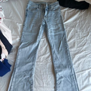 Bootcut ljusblå jeans - Säljer ett par ljusblå bootcut jeans med klassisk femficksdesign och dragkedja fram. Jeansen har en snygg, lätt utsvängd passform och är tillverkade i mjukt denimtyg som är skönt att bära. Perfekta för dig som gillar retrovibbar och vill ha en cool look.