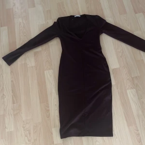 Mörklila långklänning från Zara - Säljer en stilren mörkbrun långklänning från Zara med djup v-ringning och långa ärmar. Klänningen har en slim passform och är tillverkad i mjuk polyester, perfekt för höst och vinter. Enkel design utan mönster eller extra detaljer, riktigt snygg och tidlös.