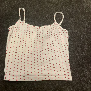 Vit linne med röda hjärtan Gina Tricot - Supersöt vit linne från Gina Tricot med tunna axelband och små röda hjärtan över hela tyget. Perfekt för varma dagar eller som ett gulligt lager under en skjorta. Mjuk och lätt i materialet, sitter skönt och har en enkel, rak passform.