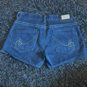 Mörkblå jeansshorts från LAB - Snygga mörkblå jeansshorts från LAB med klassisk femficksdesign och kontrastsömmar. Baksidan har coola broderade detaljer på fickorna och en patch vid linningen. Perfekta för varma dagar när du vill ha en chill och stilren look.