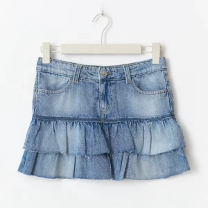 Blå jeanskjol med volanger - Supersöt kort jeanskjol i blå denim med två lager volanger och råa kanter. Klassisk femficksmodell med bälteshällor och knapp framtill. Perfekt för dig som vill ha en trendig och avslappnad look.