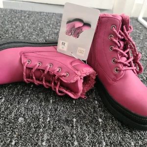 Rosa boots med foder och snörning - Snygga rosa boots från T&D med grov svart sula och matchande rosa snörning. Skorna har mjukt foder på insidan som håller dig varm och en robust design som passar perfekt till kyligare dagar.