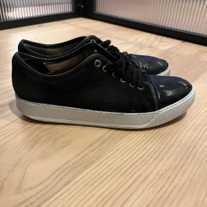 Lanvins med glans - Stilrena svarta sneakers med snygg lackad tå och vit sula. Skorna har snörning och en mix av mocka och glansigt material framtill. Perfekta för dig som gillar en clean look. Skriv om ni vill ha mer bilder eller har frågor.