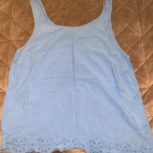 Ljusblå linnetopp från H&M Divided, M - Supersöt ljusblå linnetopp från H&M Divided i storlek 38. Toppen är ärmlös och har broderade blommiga detaljer längst ner som ger en extra touch. Perfekt för varma dagar och enkel att matcha med jeans eller kjol.