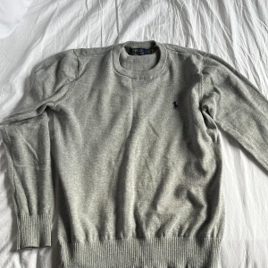 Grå tröja från Polo Ralph Lauren - Säljer en stilren grå tröja från Polo Ralph Lauren med rund hals och broderad logga på bröstet. Tröjan har långa ärmar och ribbade muddar vid ärmslut och nederkant. Perfekt för en klassisk look.