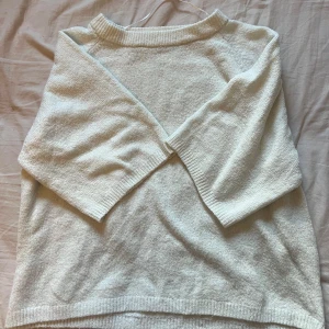 Vit stickad tröja från 157 - Mysig vit stickad tröja från 157 med rund halsringning och trekvartsärm. Tröjan har ribbade muddar vid hals, ärmslut och nederkant. Perfekt för lager-på-lager och chill dagar.