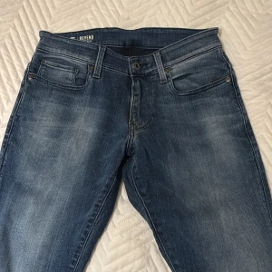 G-Star Raw Revend Slim jeans blå 29/34 - Snygga blå jeans från G-Star Raw, modell Revend Super Slim. Jeansen har klassisk femficksdesign, slitna detaljer och snygg tvätt. De är tillverkade i stretchig denim för en bekväm slim fit. Perfekta för dig som gillar en modern och stilren look.