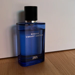 Zara Bogoss Vibrant Leather parfym - En stilren parfym från Zara, Bogoss Vibrant Leather, i en snygg blå glasflaska med svart lock och silverdetalj. Flaskan har en modern, kantig form och känns lyxig att hålla i handen. Perfekt för dig som gillar fräscha och maskulina dofter.