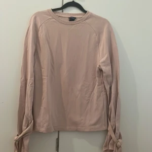 Beige långärmad tröja med knyt från Lindex - Säljer en beige långärmad tröja från Lindex i 100% bomull. Tröjan har rund halsringning och snygga knytdetaljer vid ärmsluten som ger en unik touch. Perfekt för dig som gillar stilrena plagg med en twist.