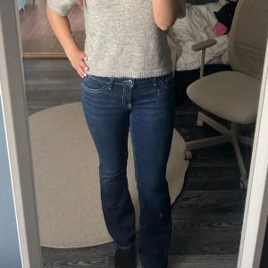 Mörkblå bootcut jeans med låg midja - Snygga mörkblå bootcut jeans med låg midja från Gina young med vita kontrastsömmar och dekorativa bakfickor med knappar. Storlek 164 med sitter som S. 