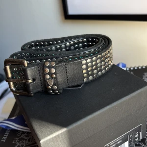Svart HTC nitarbälte i skinn - Säljer ett svart grisch bälte från HTC . Bältet är tillverkat i fint läder från italien och har en robust metallspänne med cool vintagekänsla. Perfekt till gråa eller svarta jeans. Nypris på detta bälte är cirka 2000 kr