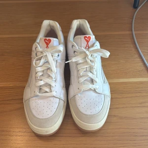 Puma x Ami Slipstream vita sneakers - Säljer ett par Puma x Ami Slipstream sneakers i vitt och beige med snygga röda Ami-hjärtan. Extra orginal röda skosnören medföljer. Ovandelen är i skinn och mocka för en clean och modern vibe. Skorna är använda endast vid två tillfällen därav mycket bra skick.
