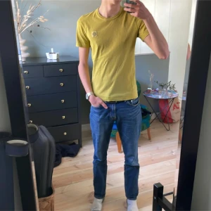 Gul t-shirt från Stone Island - Snygg gul t-shirt från Stone Island med klassisk logga på bröstet. T-shirten är i bomull och har en normal passform med korta ärmar och rund hals. Perfekt för dig som gillar streetwear och vill sticka ut med en fräsch färg.