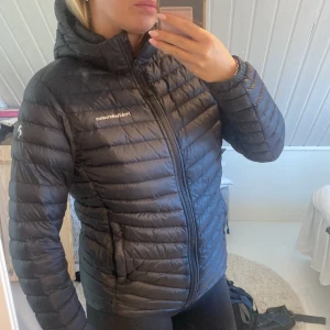 Svart dunjacka Peak Performance 170 - Säljer en svart dunjacka från Peak Performance med huva och dragkedja. Jackan är quiltad och har logga på bröstet och ärmen.  Lagning på armen se bild 3. Inte synligt