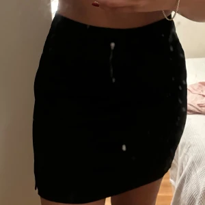 Svart tight kortkjol med slits - Svart kjol med en liten slits på sidan. Enkel och stilren design som sitter snyggt och går att skapa många outfits. Perfekt för dig som gillar minimalistisk stil och vill ha en kjol som är lätt att matcha. Funkar både festligt och vardagligt. 