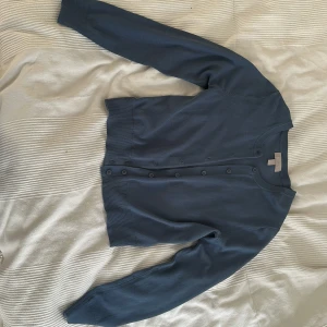 Mörkblå kofta med knappar - En stilren mörkblå kofta med rund hals och knäppning framtill. Tröjan har långa ärmar och ribbade muddar vid ärmslut och nederkant. Perfekt att slänga över en t-shirt eller linne för en chill look.