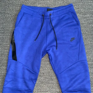 Blå mjukisbyxor från Nike, Pris kan diskuteras  - Snygga blå mjukisbyxor från Nike i storlek L passar M. Byxorna har svarta snören i midjan, svarta detaljer vid fickorna och Nike-logga på vänster ben. Tillverkade i mjukt bomullsmaterial, perfekt för chill eller träning. Modern passform med ribbade benslut.