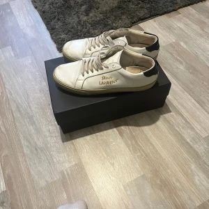 Saint Laurent Skor - Säljer ett par vita Saint Laurent sneakers med guldfärgad logga. Dom är köpa på vesitare colletion och använda ca 10 månader. Ett par lite unikare Saint Laurents. Fler bilder kan fås! Sulan är bytt. Hör av er vid frågor!