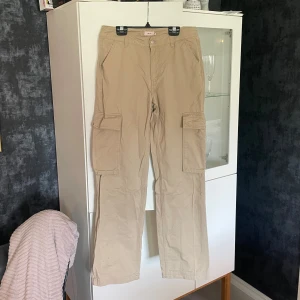 Beige cargopants från Nelly - Snygga beige cargopants från Nelly med tight midja, raka/vida ben och stora fickor på sidorna. Snygga på! Använda vid 1 tillfälle - så i stort sett helt nytt skick. 